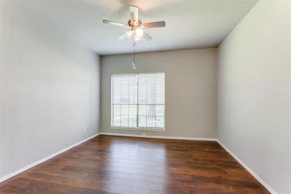 an empty room with wooden floor chandelier fan and windows