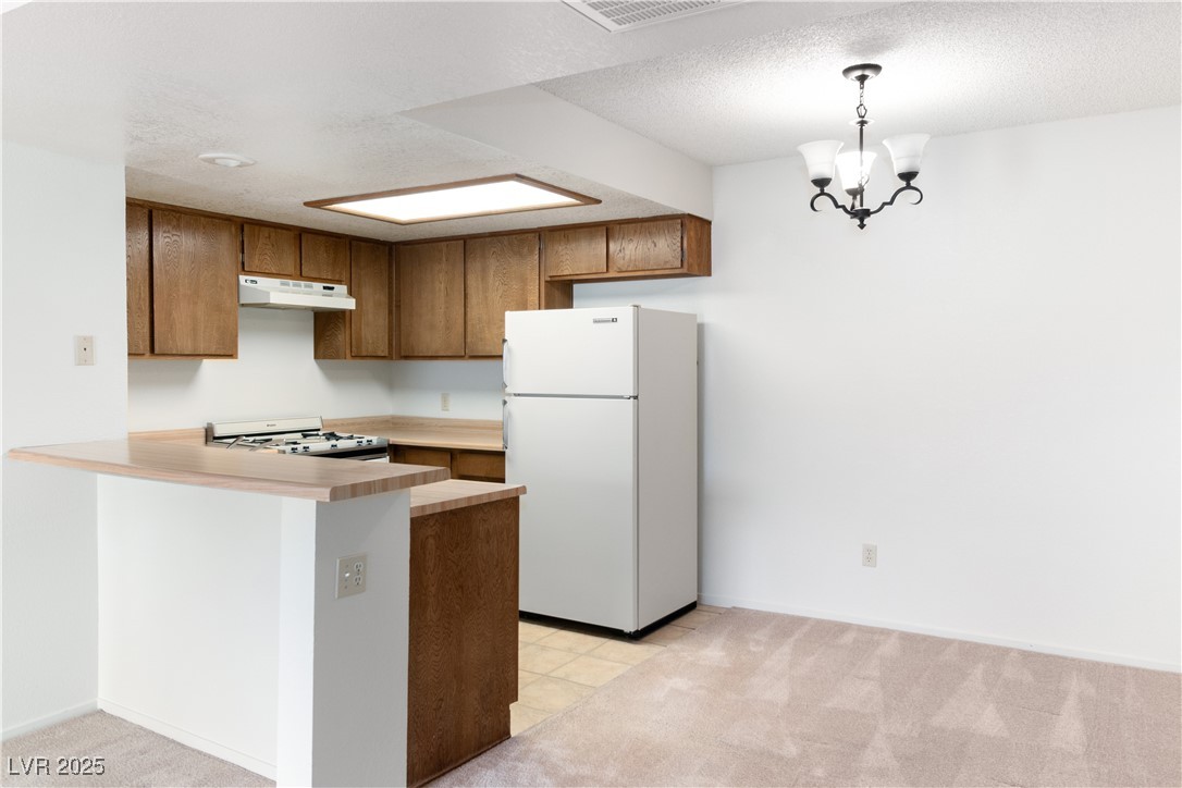 3740 Desert Marina Drive, Unit 2 Laughlin, NV 89029 - Photo 11 of 75 Kitchen featuring light countertops, white appliances, a peninsula, brown cabinets, and light colored carpet