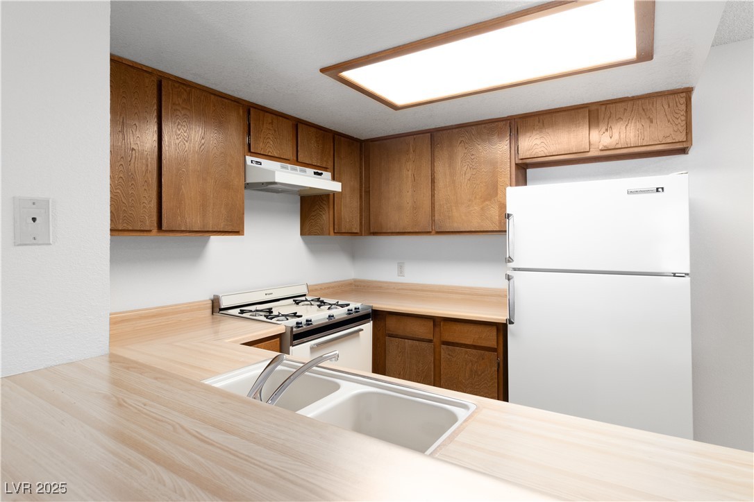 3740 Desert Marina Drive, Unit 2 Laughlin, NV 89029 - Photo 17 of 75 Kitchen with light countertops, white appliances, brown cabinets, and under cabinet range hood