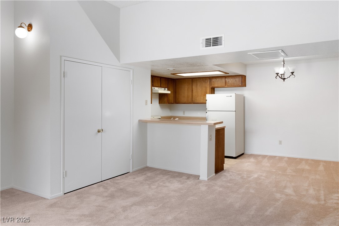 3740 Desert Marina Drive, Unit 2 Laughlin, NV 89029 - Photo 10 of 75 Living room to Kitchen with brown cabinetry, freestanding refrigerator, light carpet, light countertops, and a peninsula