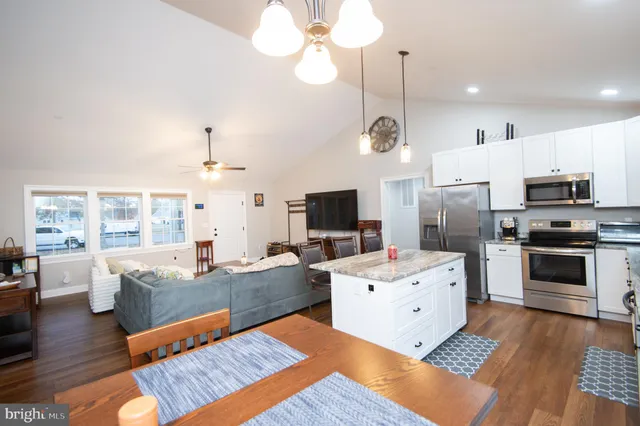 a large living room with stainless steel appliances kitchen island granite countertop a stove a sink dishwasher a dining table and chairs with wooden floor