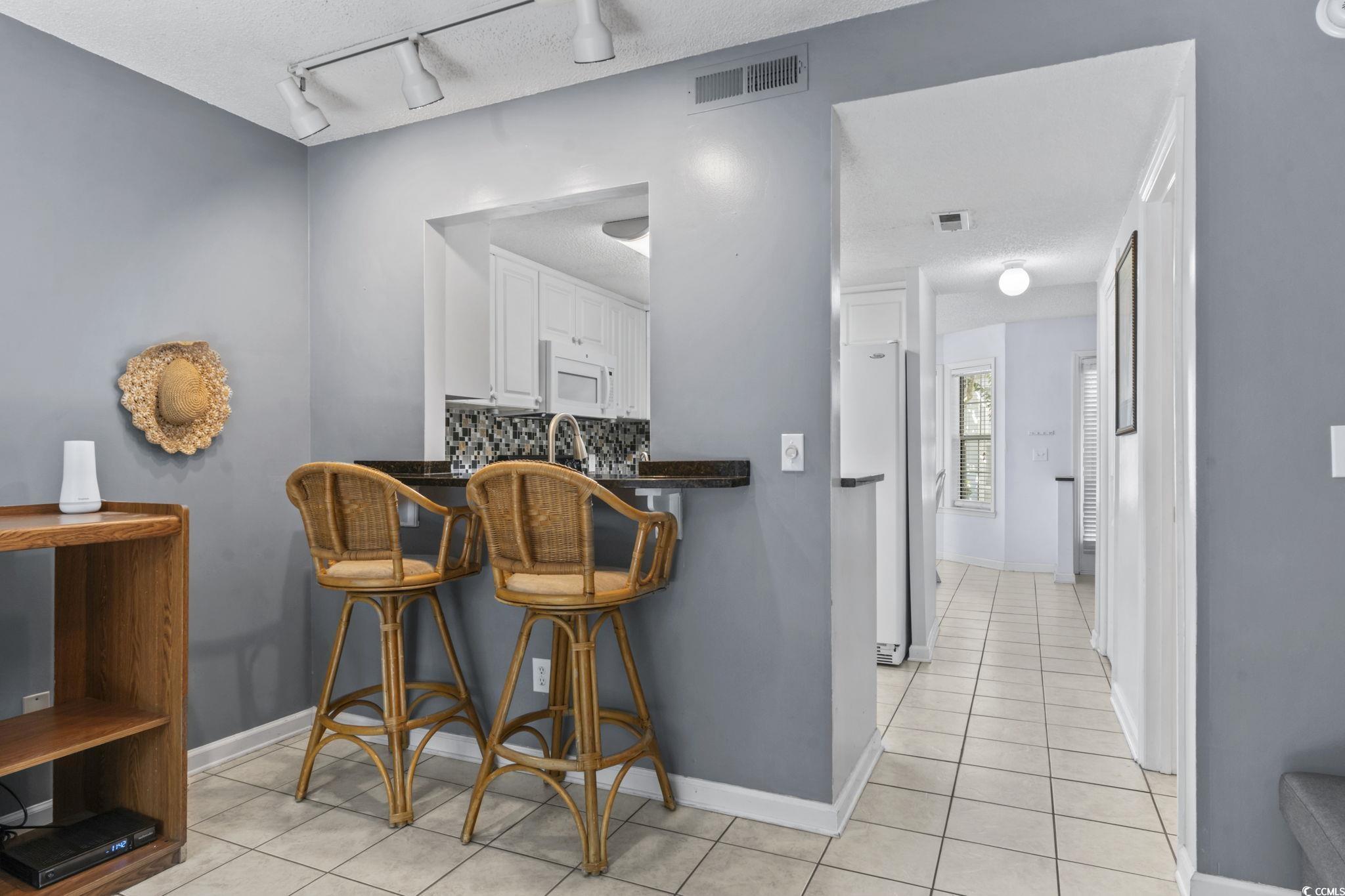 712 67th Avenue North, Unit 2A Myrtle Beach, SC 29572 - Photo 7 of 30 Kitchen with dark countertops, white cabinets, rail lighting, tasteful backsplash, and light tile patterned floors