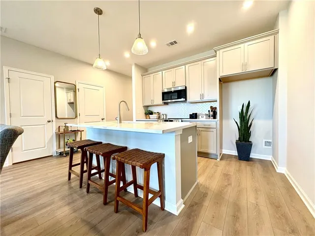 a kitchen with stainless steel appliances kitchen island granite countertop a dining table chairs and a refrigerator