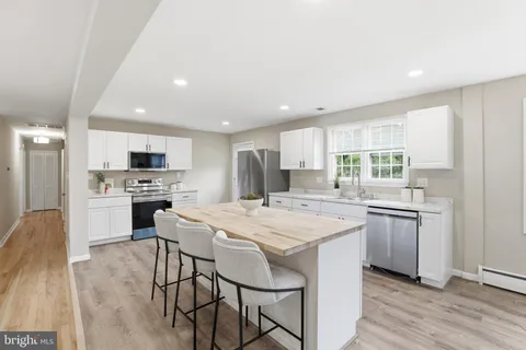 a kitchen with stainless steel appliances kitchen island granite countertop a stove a sink a refrigerator and white cabinets with wooden floor