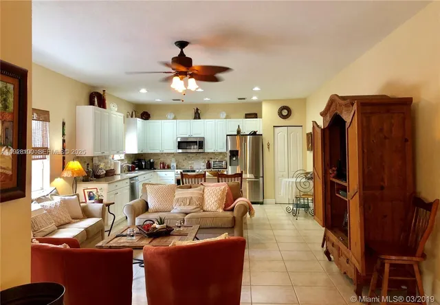 a living room with stainless steel appliances furniture a rug and a kitchen view