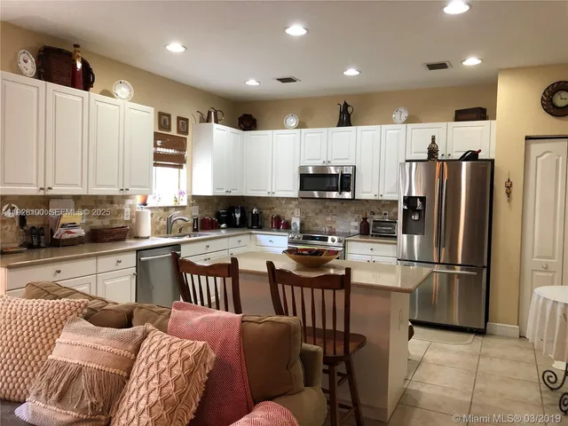 a kitchen with stainless steel appliances granite countertop a refrigerator a stove a sink a dining table and chairs