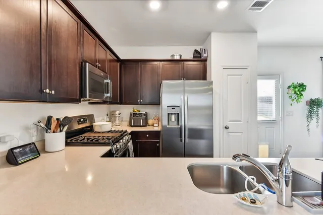 a kitchen with stainless steel appliances a sink a stove a refrigerator cabinets and a dining table