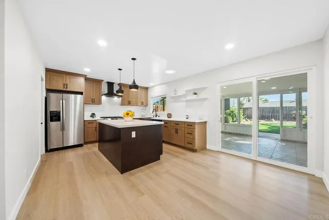 a large kitchen with a large counter top a refrigerator a sink stainless steel appliances and cabinets