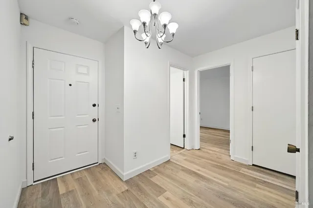 a view of an empty room with chandelier fan and wooden floor
