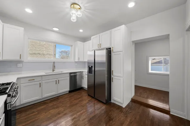 a kitchen with stainless steel appliances granite countertop a refrigerator a sink dishwasher a stove and white countertops with wooden floor