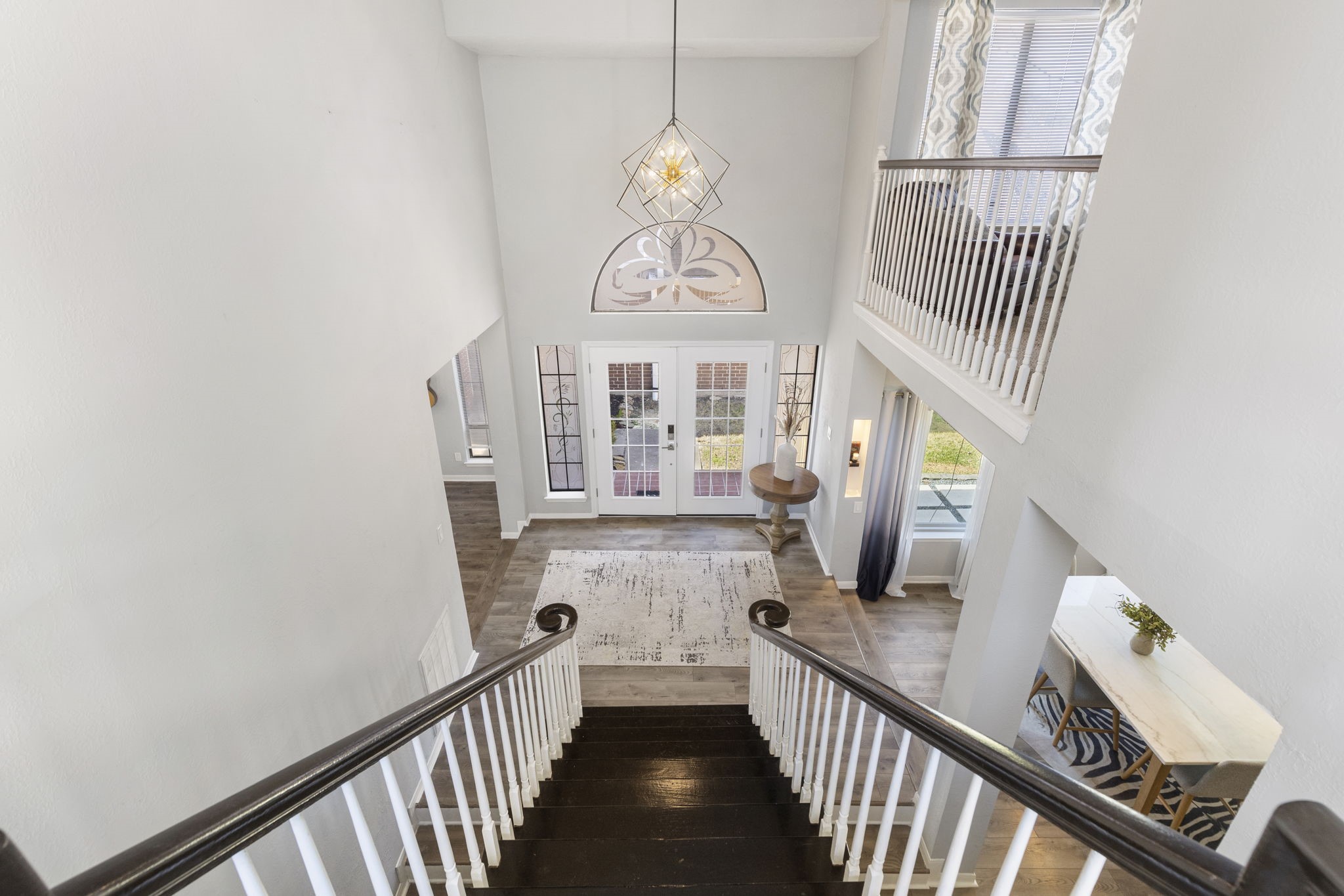 2110 Paso Rello Drive Houston, TX 77077 - Photo 22 of 41 This photo showcases a bright, welcoming foyer with high ceilings and an elegant chandelier. The staircase features dark wood steps and white railings, leading to a spacious entryway with large windows and French doors that offer ample natural light. The open layout provides a glimpse into adjacent rooms, enhancing the home's airy feel.