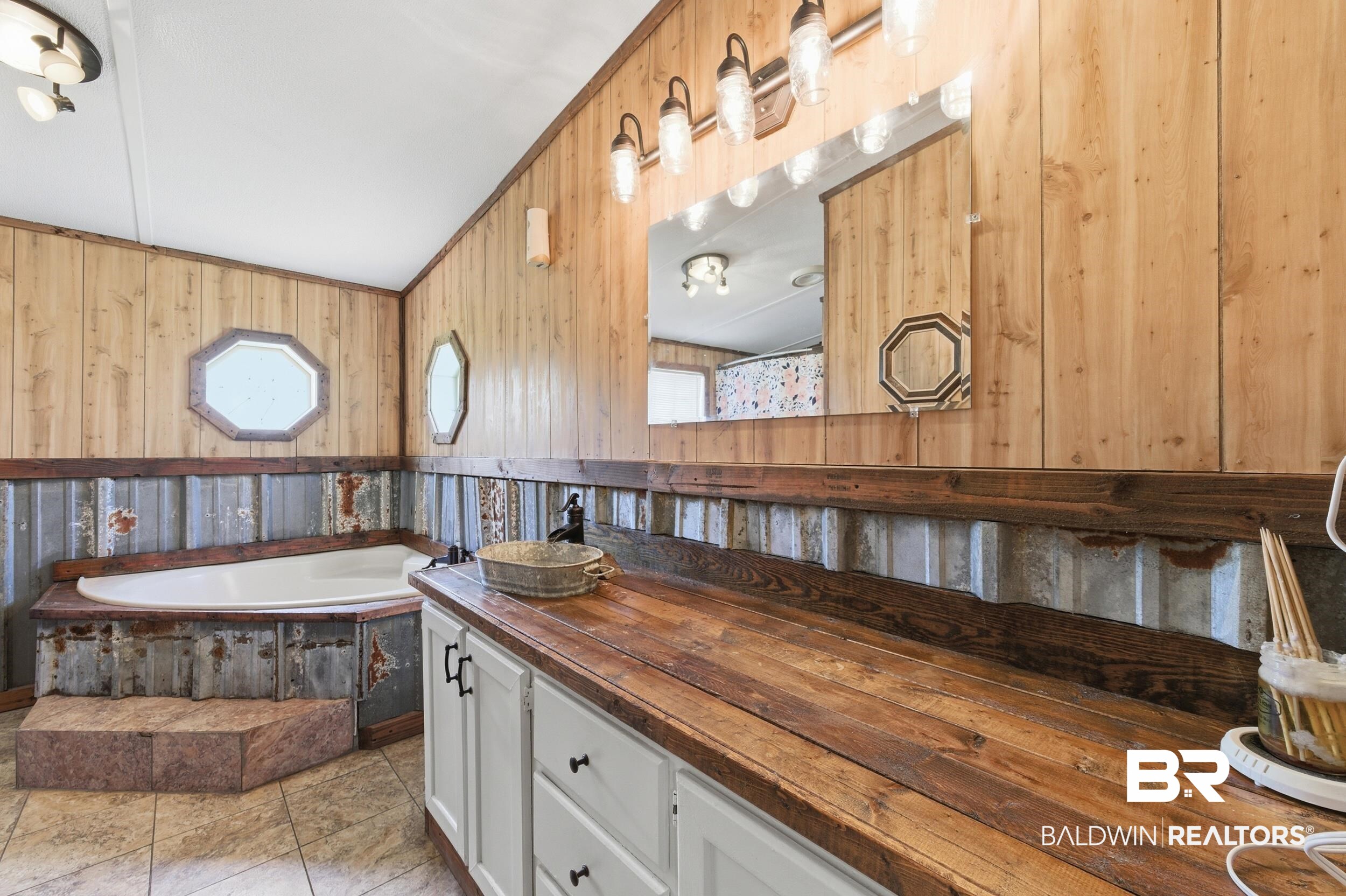 926 Tumbling Lane Atmore, AL 36502 - Photo 29 of 56 Spacious bathroom featuring an angular soaking tub with built-in steps, wood-paneled walls, and a large vanity with a wood-finish countertop
