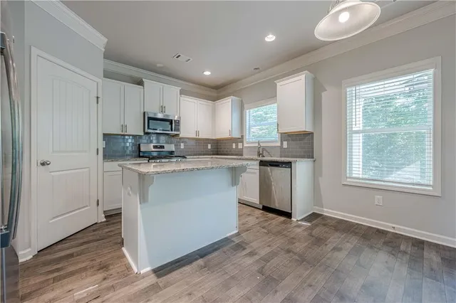 a kitchen with stainless steel appliances granite countertop a stove a sink a refrigerator white cabinets and a window