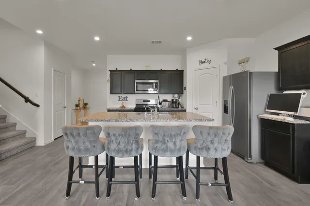 a kitchen with stainless steel appliances granite countertop a dining table chairs refrigerator and microwave