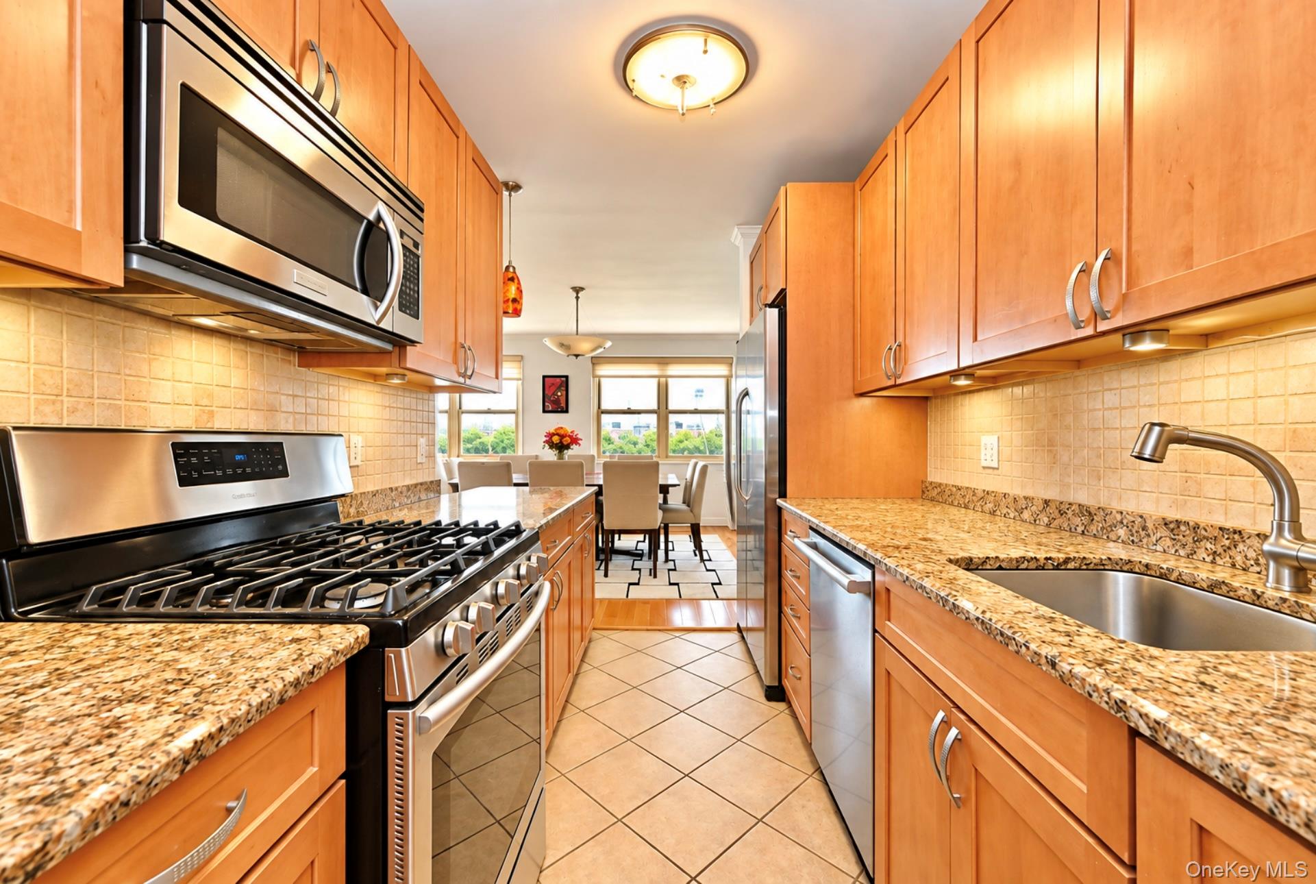102-30 66th Road, Unit 17E Queens, NY 11375 - Photo 4 of 21 Galley kitchen featuring stainless steel appliances, light wood-finish cabinetry, granite countertops, and tiled flooring