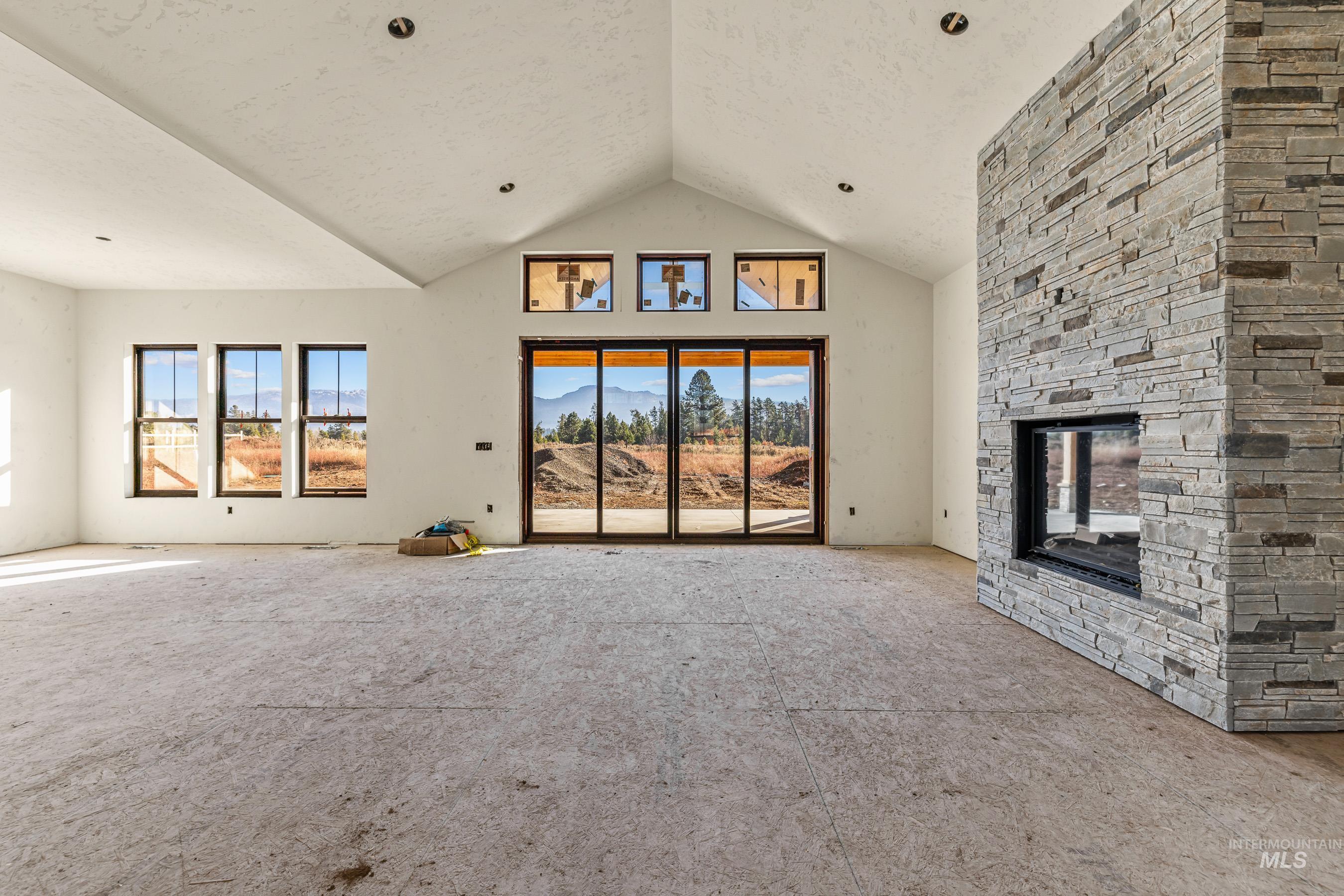 13910 Sky View Court, Unit 8 McCall, ID 83638 - Photo 7 of 40 Unfurnished living room with a mountain view, a stone fireplace, high vaulted ceiling, a textured ceiling, and carpet floors