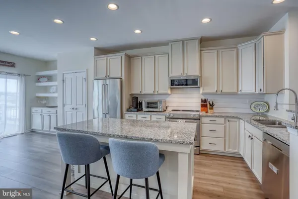 a kitchen with stainless steel appliances granite countertop a stove a sink dishwasher a refrigerator and white cabinets with wooden floor