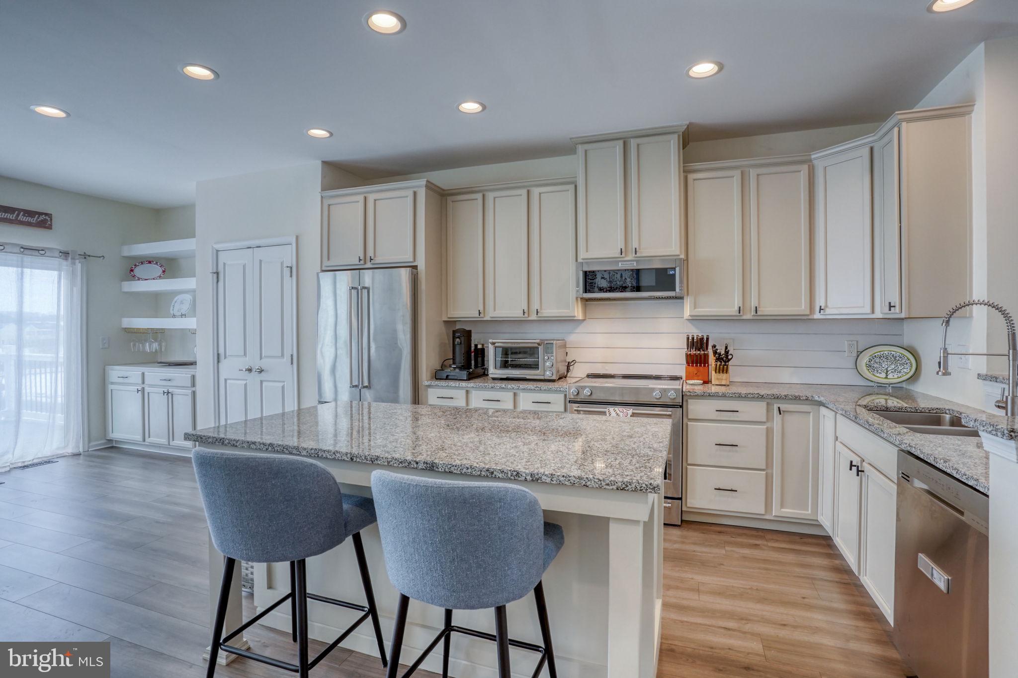 a kitchen with stainless steel appliances granite countertop a stove a sink dishwasher a refrigerator and white cabinets with wooden floor