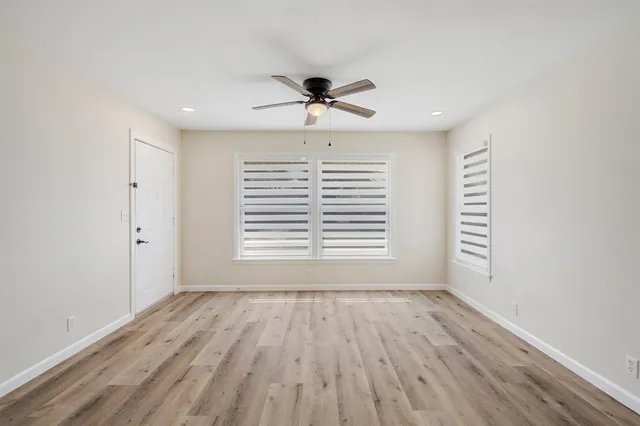 an empty room with wooden floor chandelier fan and windows