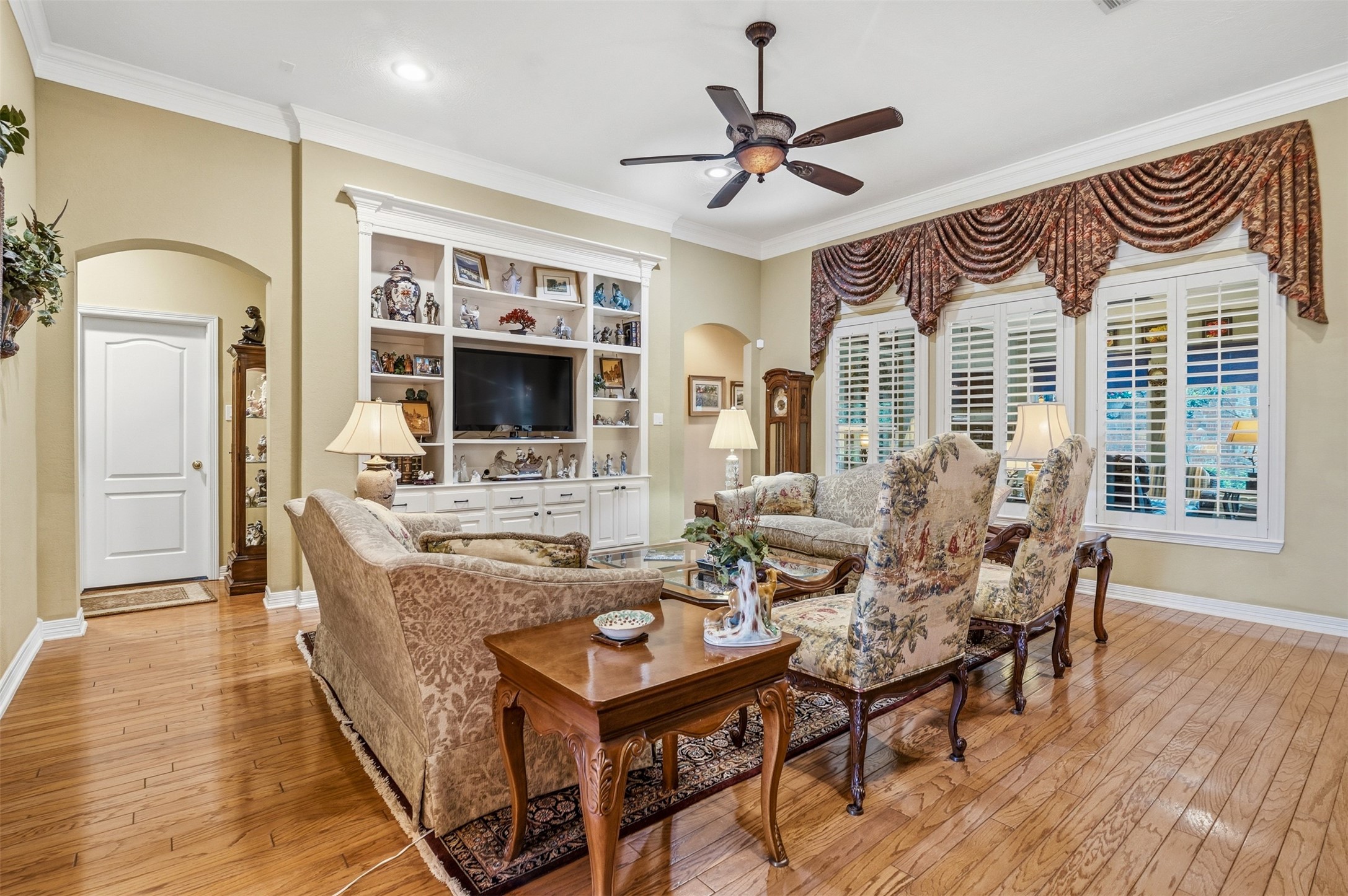 12215 Pebble Meadows Houston, TX 77041 - Photo 9 of 44 The family room features wood floors, ceiling fan, wall of windows with shutters and custom built ins with storage space.