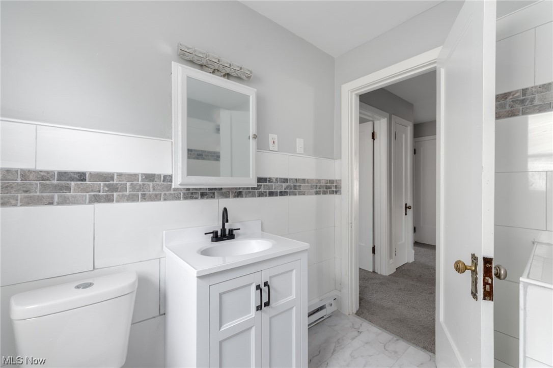 1228 Melbourne Road Cleveland, OH 44112 - Photo 15 of 35 Bathroom featuring vanity, tile walls, a baseboard heating unit, toilet, and tile floors