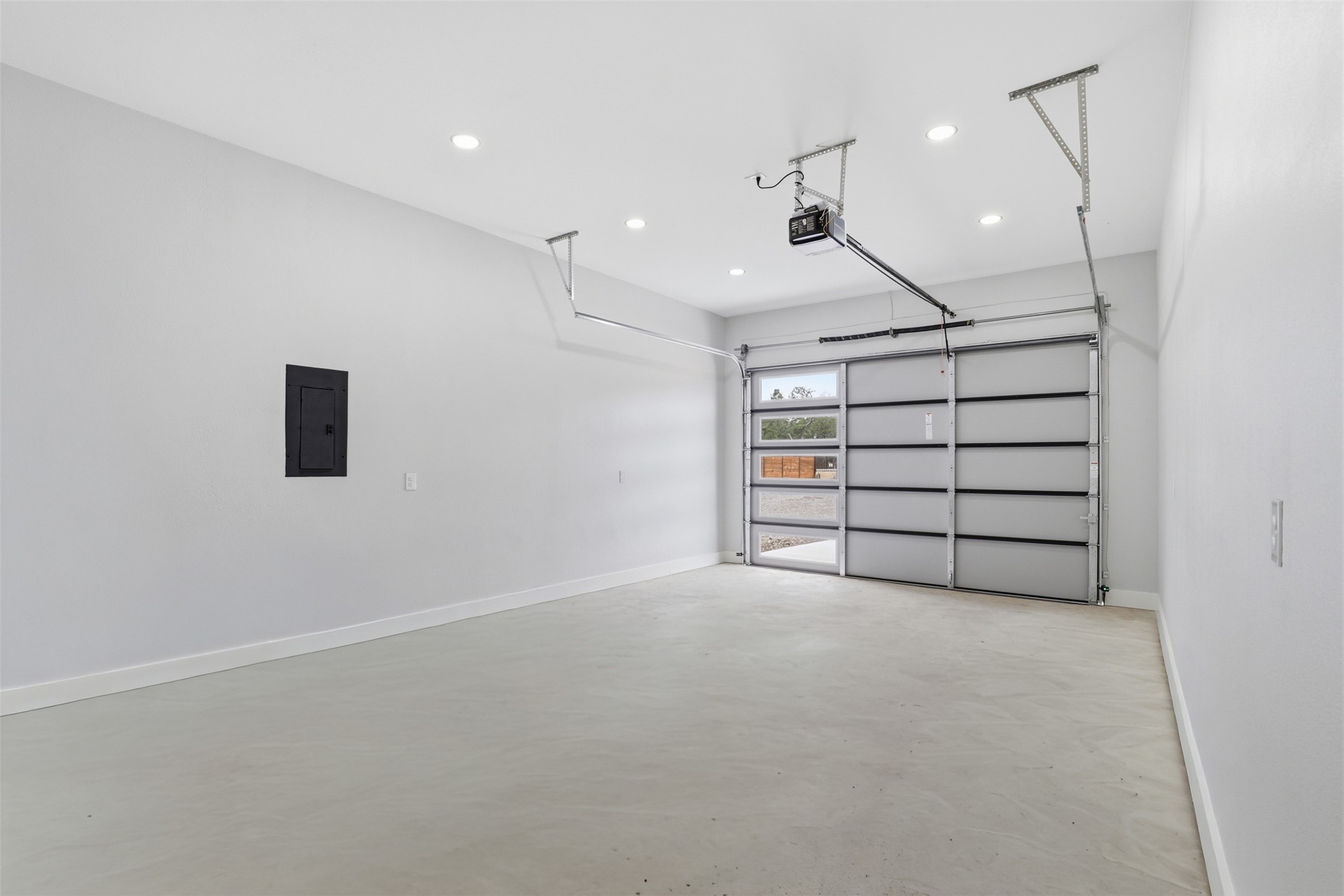 123 Los Robles Road Elgin, TX 78621 - Photo 20 of 21 Spacious garage featuring a light gray concrete floor, white walls, recessed ceiling lighting, and a modern glass-paneled garage door with an automatic opener