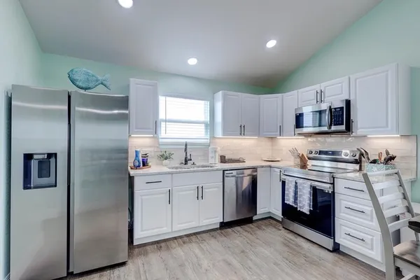 a kitchen with stainless steel appliances granite countertop white cabinets a sink a stove a refrigerator and island with wooden floor