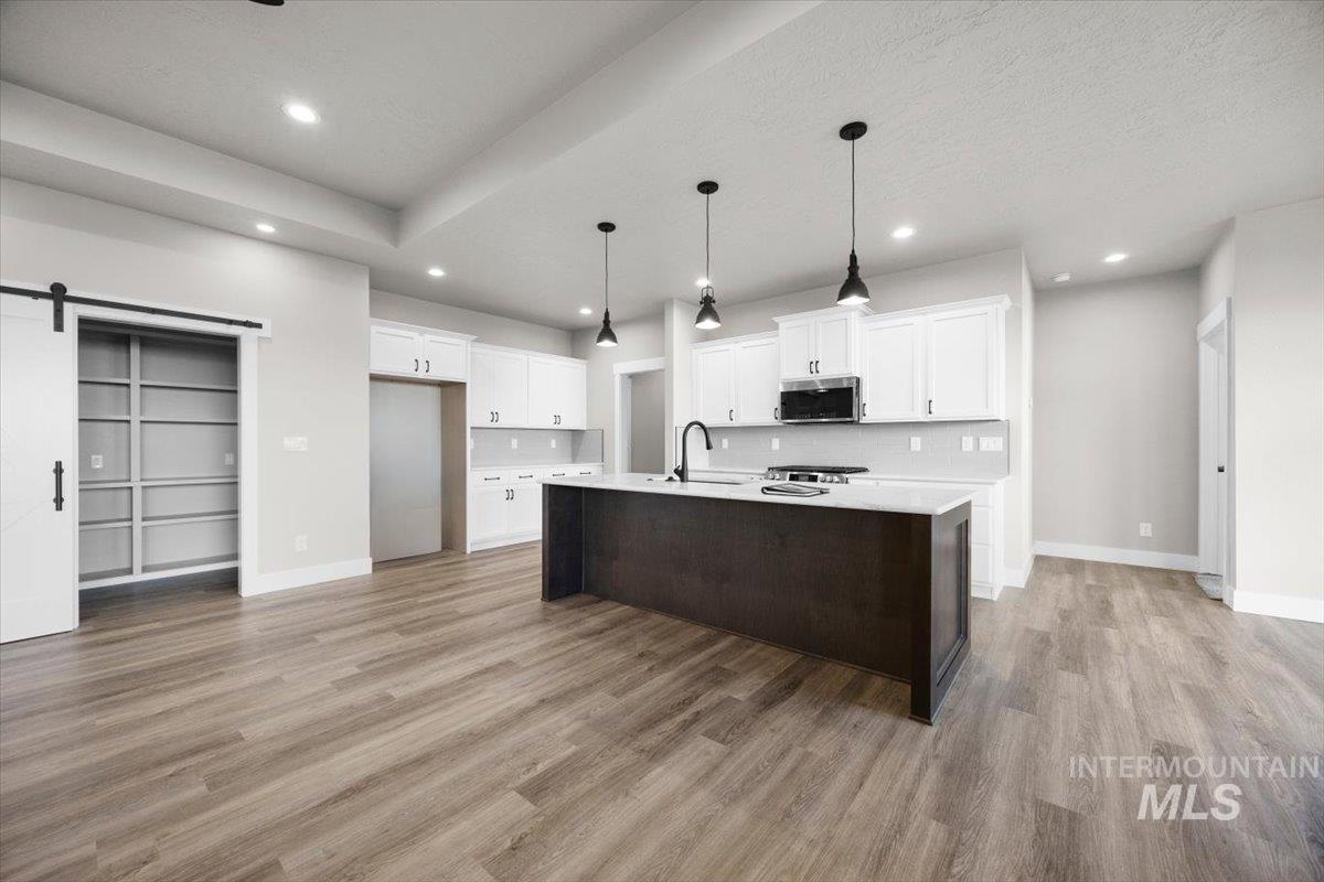103 Ash Street Parma, ID 83660 - Photo 2 of 22 Two tone kitchen featuring a barn door, a kitchen island with sink, dark wood-type flooring, hanging light fixtures, and stainless steel microwave