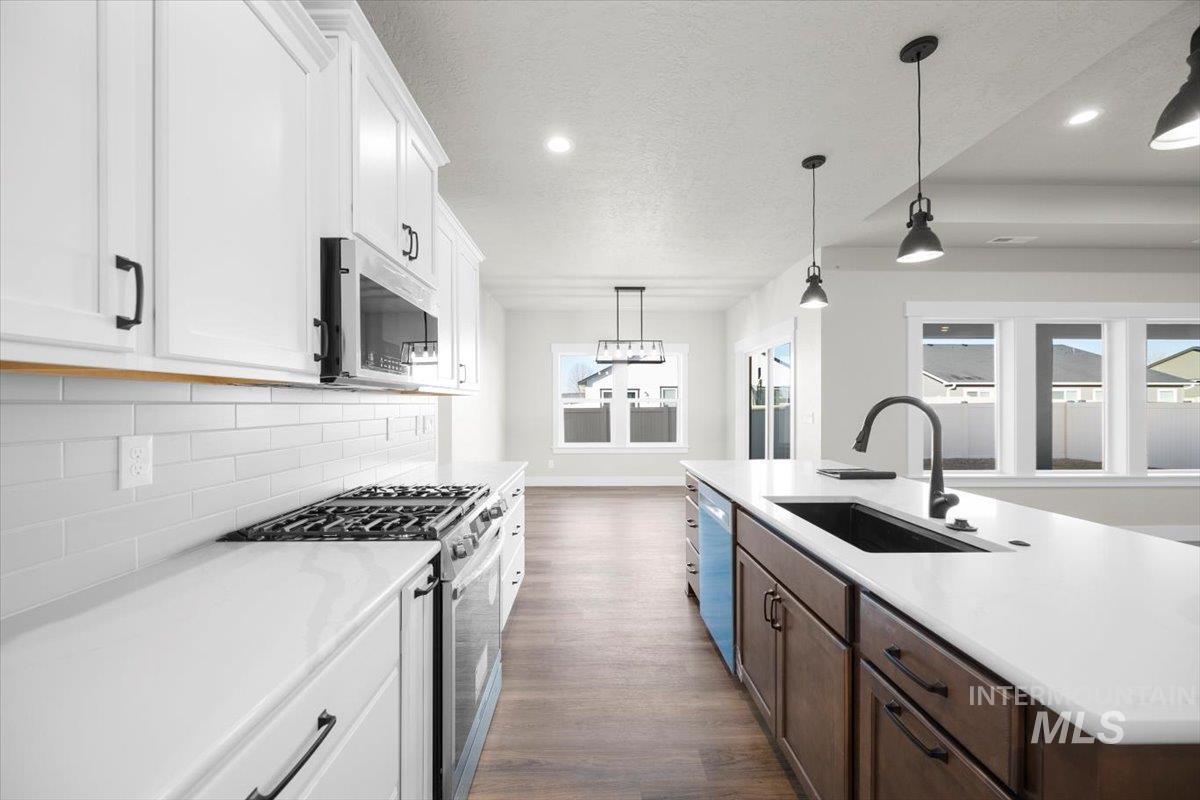 103 Ash Street Parma, ID 83660 - Photo 3 of 22 Two tone kitchen featuring two tone color scheme, stainless steel appliances, pendant lighting, a center island with sink, and dark wood-type flooring