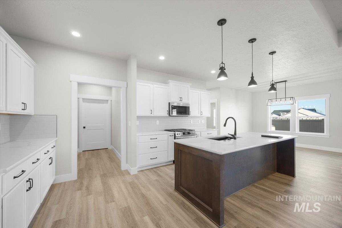 103 Ash Street Parma, ID 83660 - Photo 4 of 22 Two tone kitchen with decorative light fixtures, light wood finished floors, tasteful backsplash, an island with sink, and two tone cabinetry