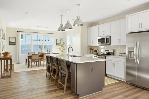 a kitchen with stainless steel appliances granite countertop a refrigerator a stove a sink a dining table and chairs with wooden floor