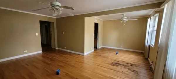 a view of an empty room with wooden floor and a ceiling fan