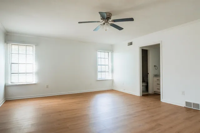 an empty room with wooden floor fan and windows