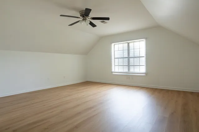 an empty room with wooden floor fan and windows
