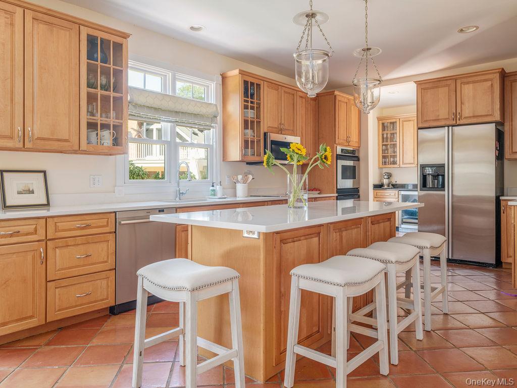 10947 North Bayview Road Southold, NY 11971 - Photo 26 of 43 Kitchen featuring a breakfast bar area, stainless steel appliances, light tile patterned flooring, glass insert cabinets, and decorative light fixtures