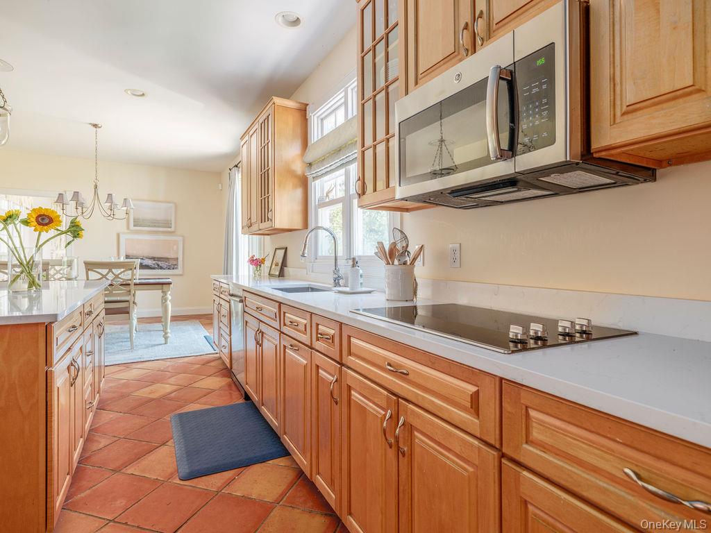 10947 North Bayview Road Southold, NY 11971 - Photo 27 of 43 Kitchen featuring glass insert cabinets, light tile patterned floors, stainless steel microwave, hanging light fixtures, and light stone countertops