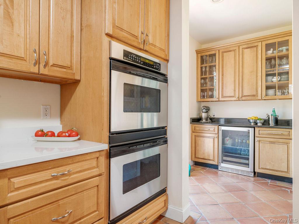 10947 North Bayview Road Southold, NY 11971 - Photo 28 of 43 Kitchen featuring stainless steel double oven, wine cooler, light tile patterned flooring, glass insert cabinets, and light brown cabinets