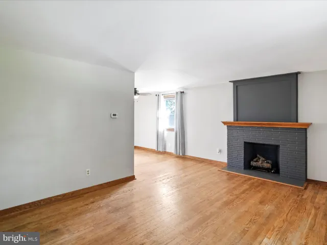 a view of an empty room with wooden floor fireplace and a window