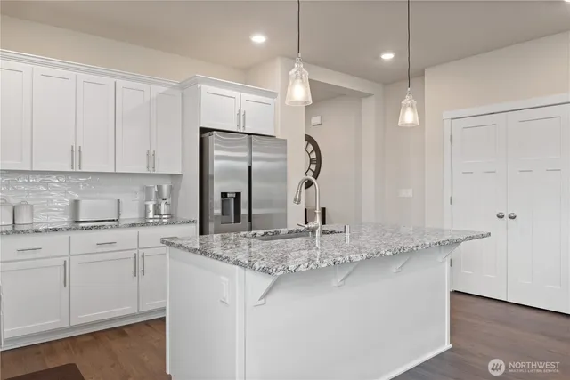 a kitchen with stainless steel appliances granite countertop a sink a refrigerator and white cabinets