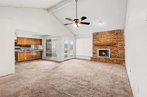 a view of a livingroom with a fireplace a ceiling fan a kitchen microwave and a refrigerator