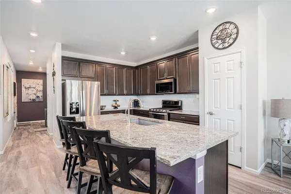 a kitchen with stainless steel appliances granite countertop a stove top oven a refrigerator a dining table and chairs with wooden floor