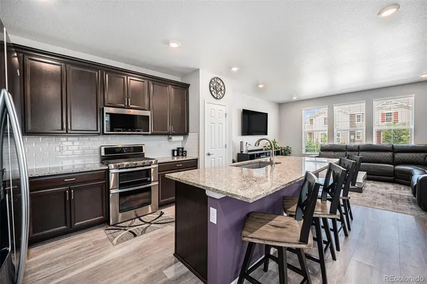 a open kitchen with stainless steel appliances granite countertop a stove top oven a sink dishwasher a dining table and chairs with wooden floor