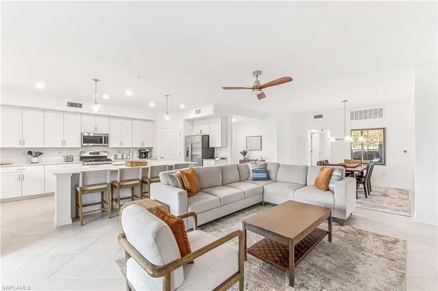 a living room with white couches and kitchen view with wooden floor