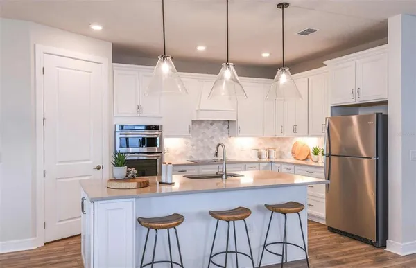 a kitchen with stainless steel appliances granite countertop a refrigerator a sink dishwasher a stove a dining table and chairs with wooden floor