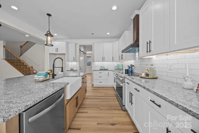 a large kitchen with stainless steel appliances granite countertop a sink dishwasher a stove and white cabinets with wooden floor