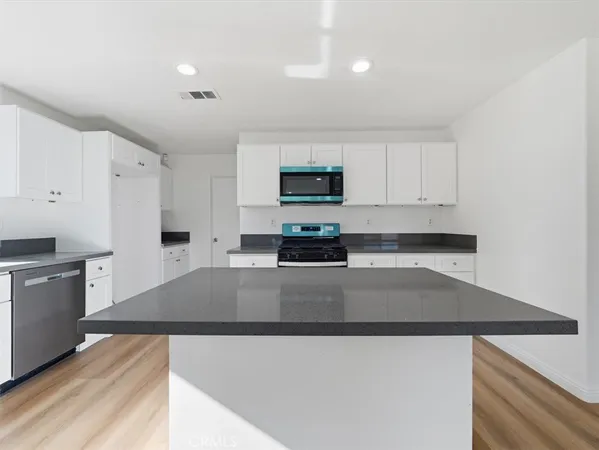 an empty room with wooden floor and kitchen view