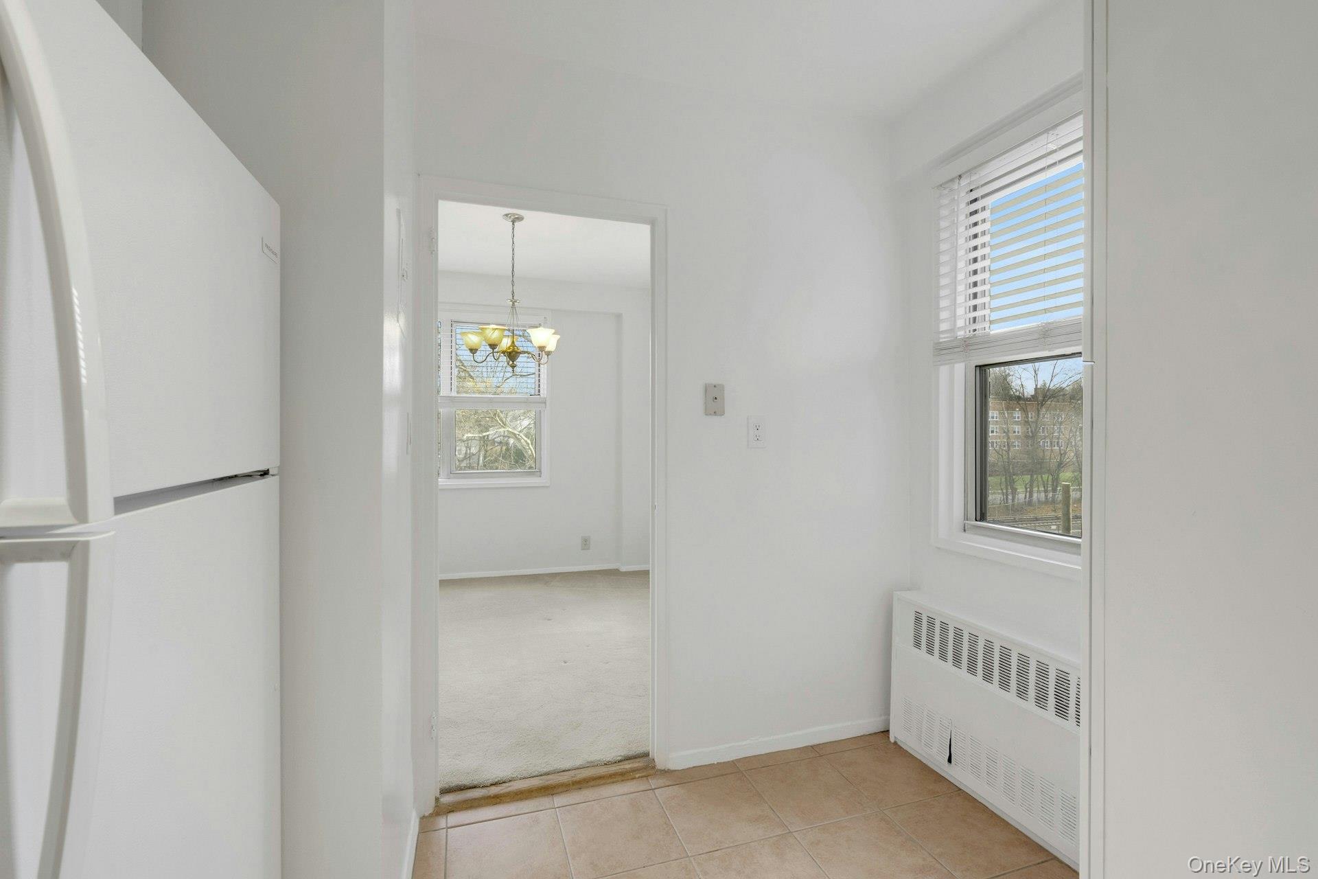 260 Garth Road, Unit 4E4 Scarsdale, NY 10583 - Photo 12 of 29 Hallway featuring radiator heating unit, a chandelier, light tile patterned floors, and light colored carpet