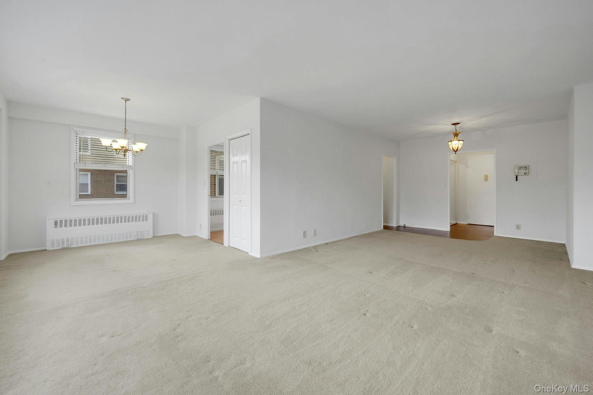260 Garth Road, Unit 4E4 Scarsdale, NY 10583 - Photo 15 of 29 Unfurnished living room with a chandelier, radiator, and light carpet