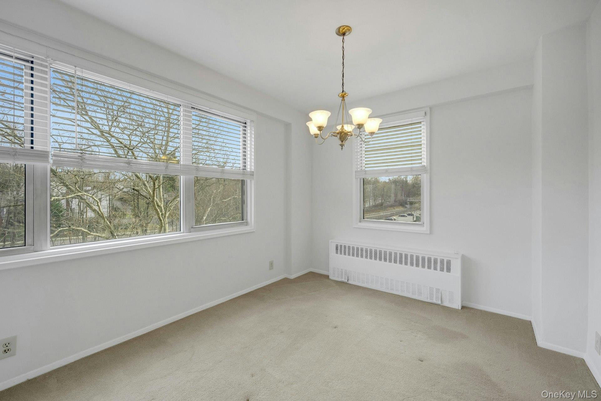 260 Garth Road, Unit 4E4 Scarsdale, NY 10583 - Photo 16 of 29 Unfurnished room with radiator heating unit, light carpet, and a chandelier