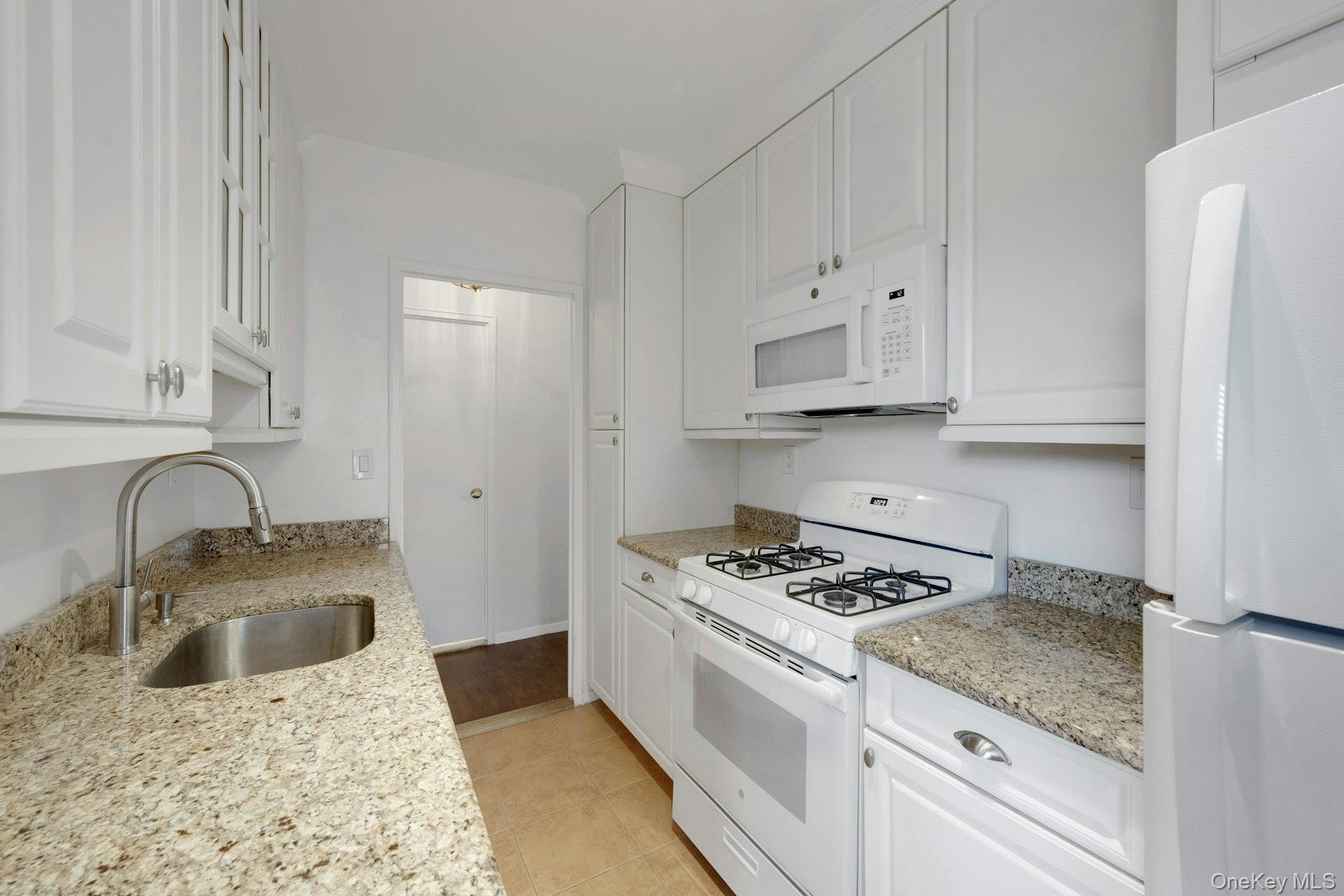 260 Garth Road, Unit 4E4 Scarsdale, NY 10583 - Photo 9 of 29 Kitchen with white appliances, white cabinetry, light stone counters, and light tile patterned floors